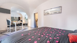 Une chambre à coucher avec un lit recouvert de pétales de rose, un miroir au mur et un coin repas agrémenté d’un lustre.