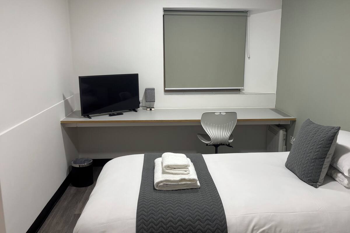 A hotel room with a bed, a desk with a computer, a chair, and a window.