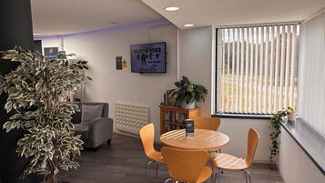 A modern room with a round table, two chairs, a potted plant, a radiator, and a window with blinds.