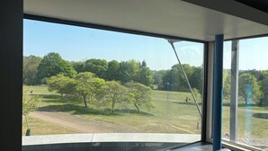 A view from a room with large windows overlooking a park with trees and a grassy area. - Broadview Hotel (Norwich)