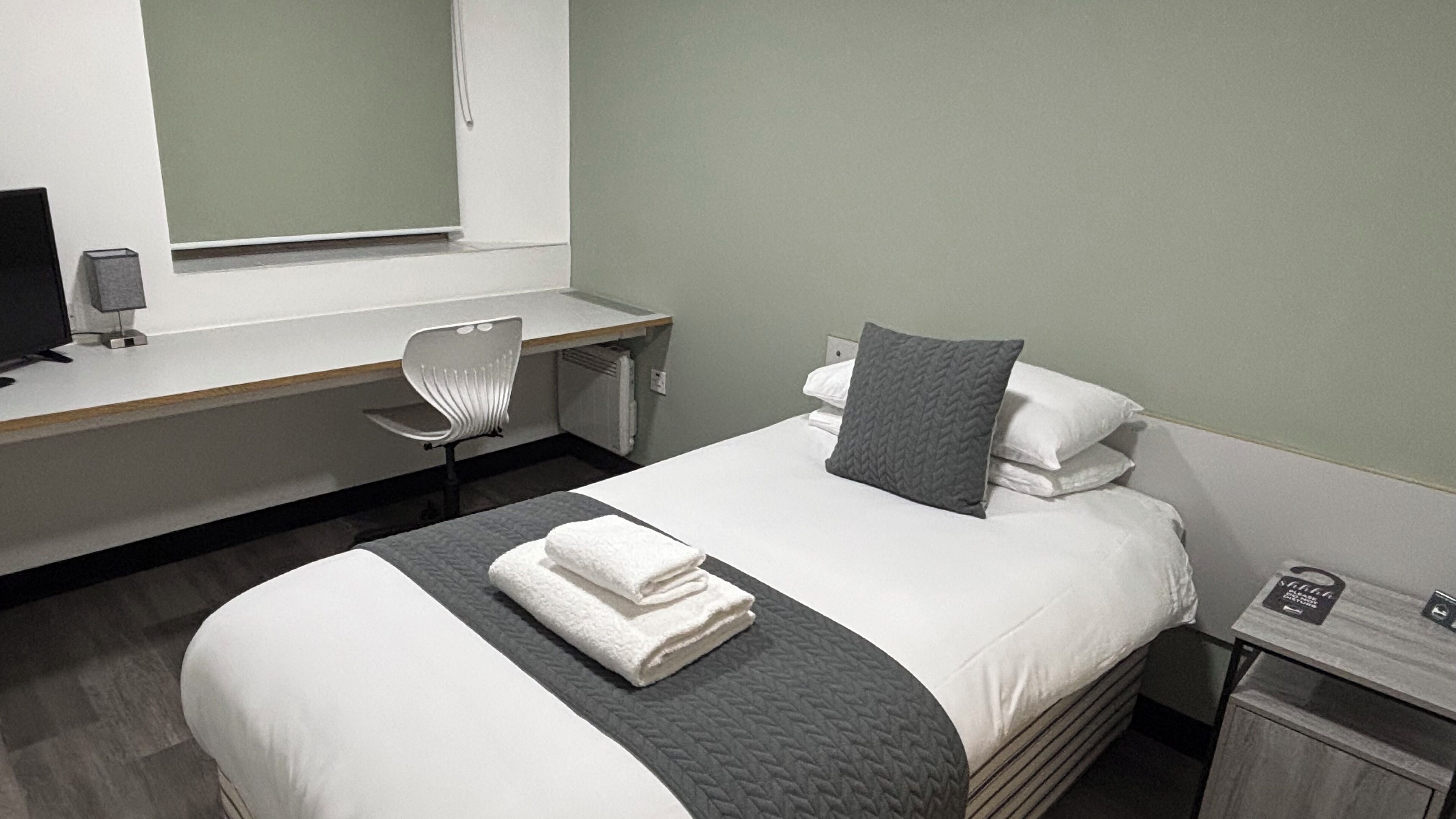 A hotel room with a bed, a desk, a chair, and a small table.