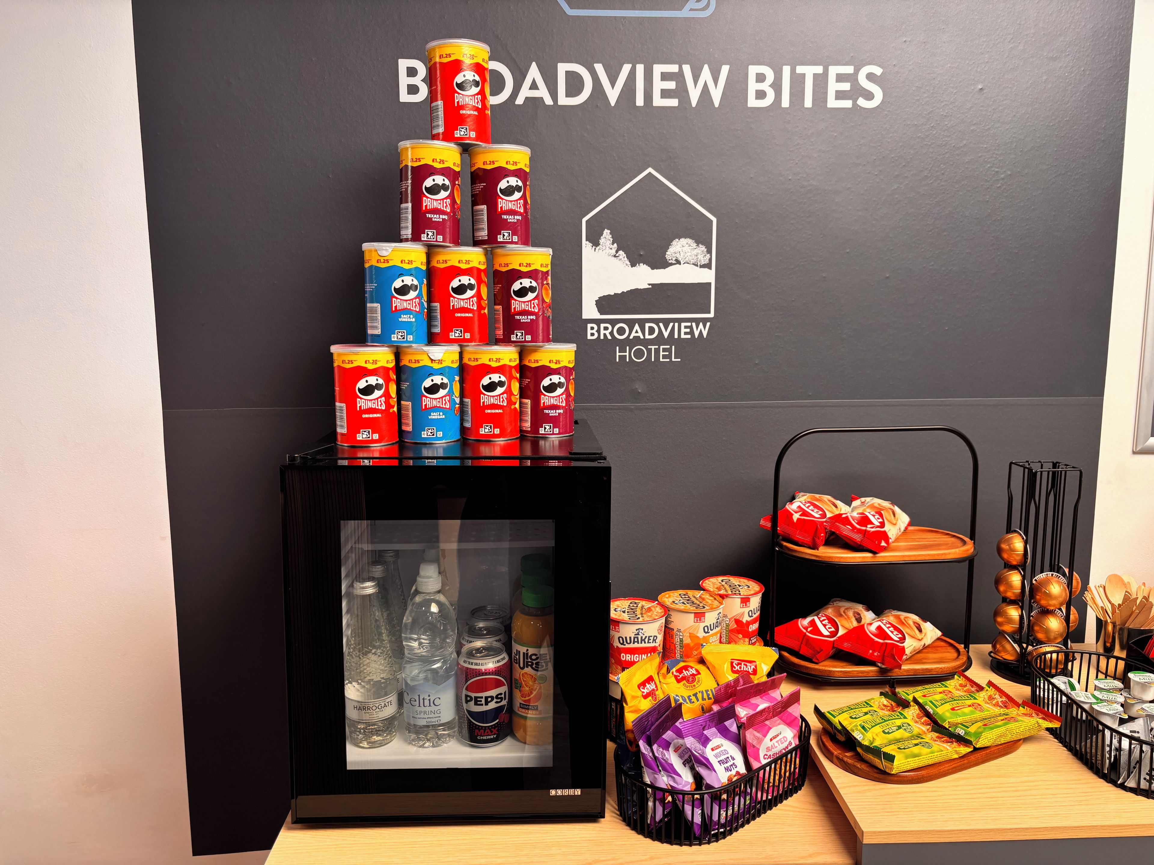 Exhibición de snacks con latas de Pringles, agua embotellada y paquetes de comida en un hotel.
