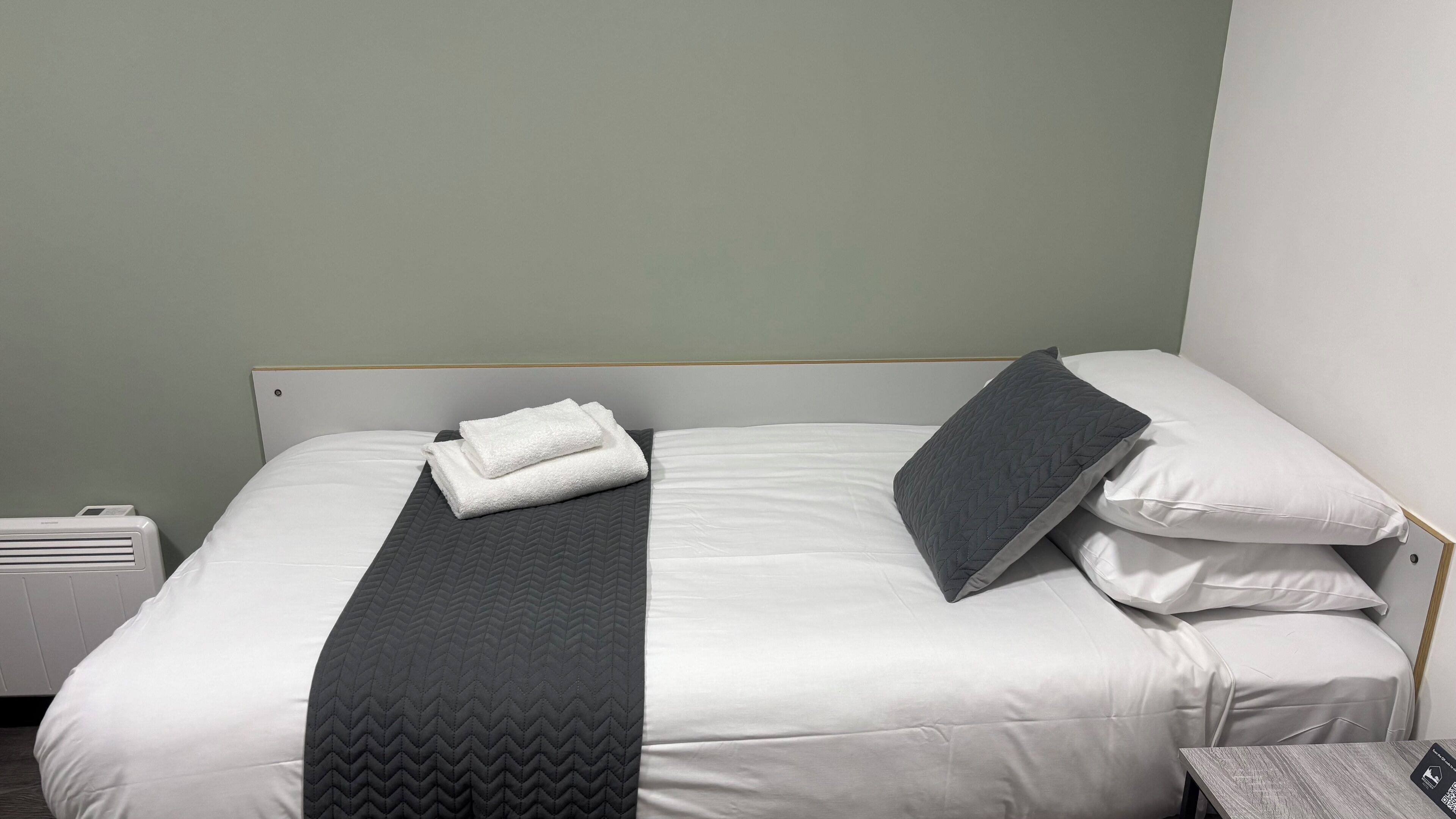A neatly made bed with white linens, a grey quilted bedspread, and a grey pillow.