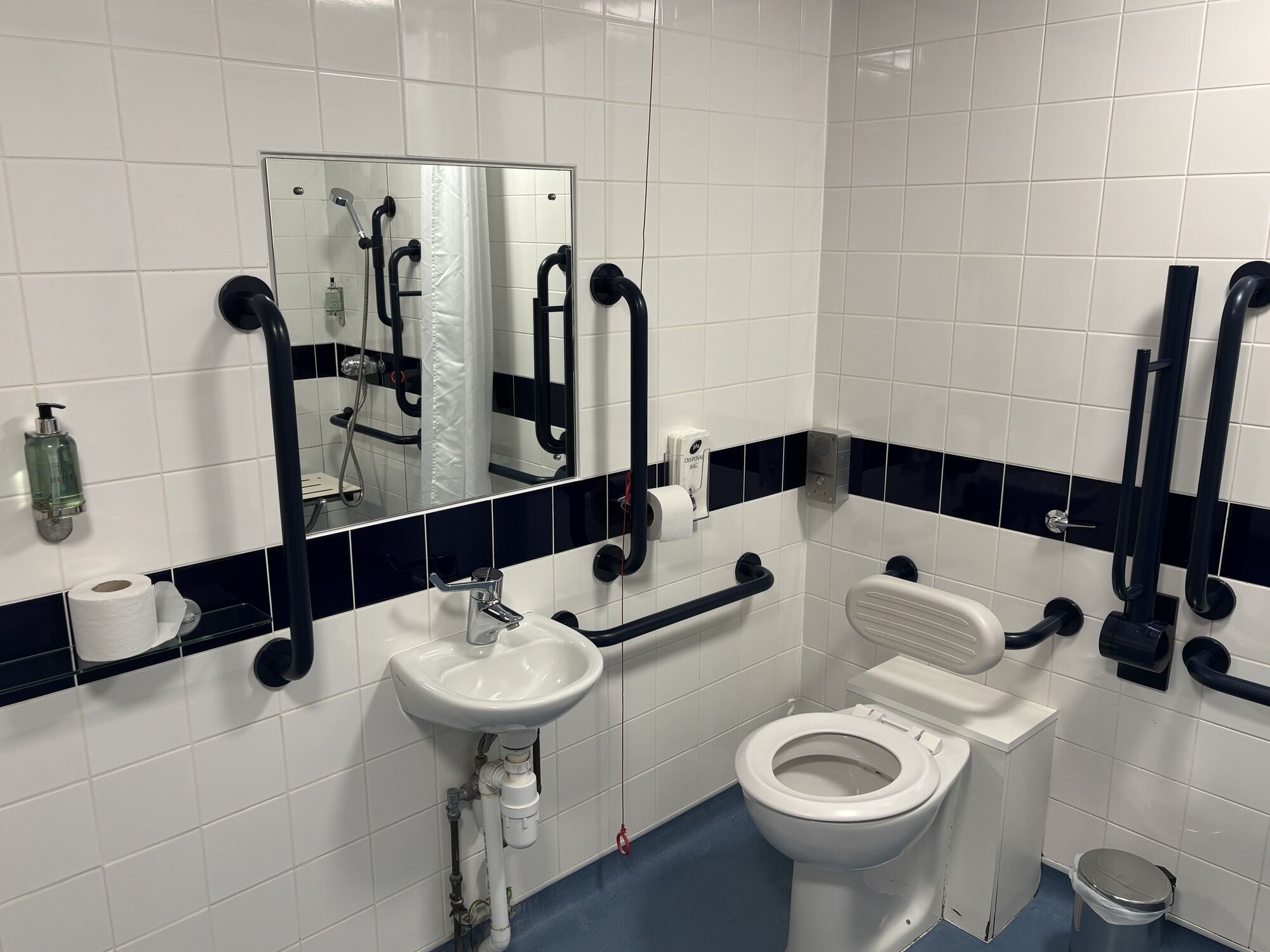 Een badkamer met witte tegels, een wastafel, toilet, spiegel en douche.