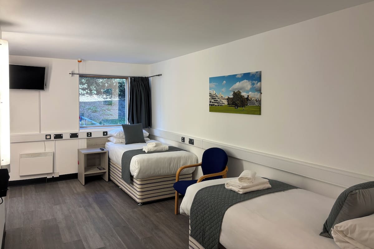 A hotel room with a bed, a desk, a chair, a TV, and a window with curtains.