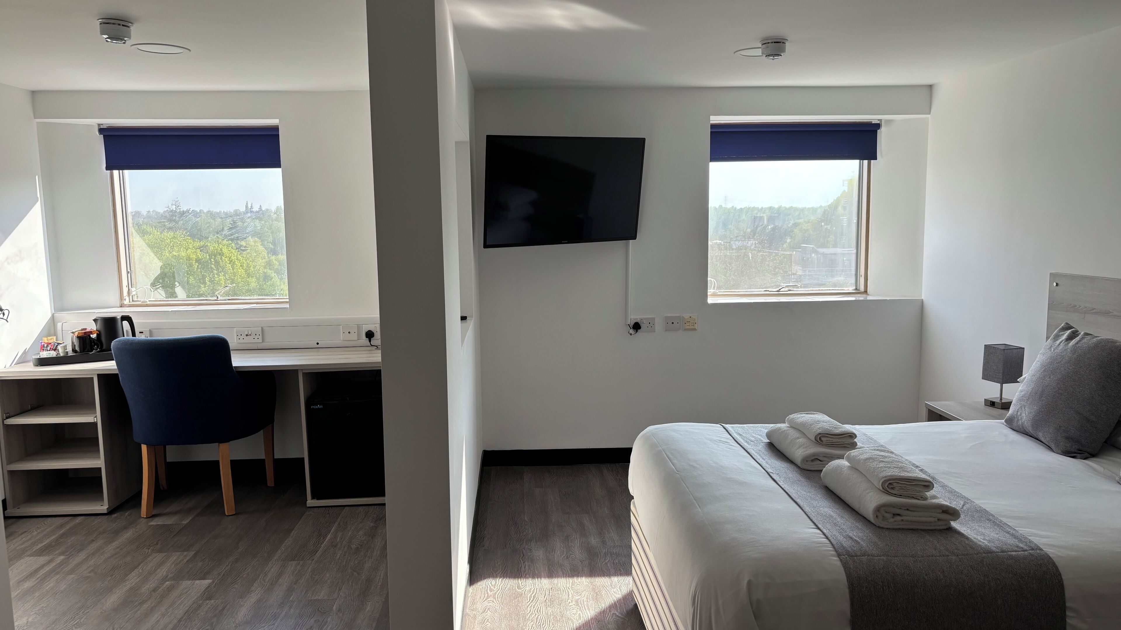 A hotel room with a bed, a desk, a chair, a TV, and a view of the outdoors.
