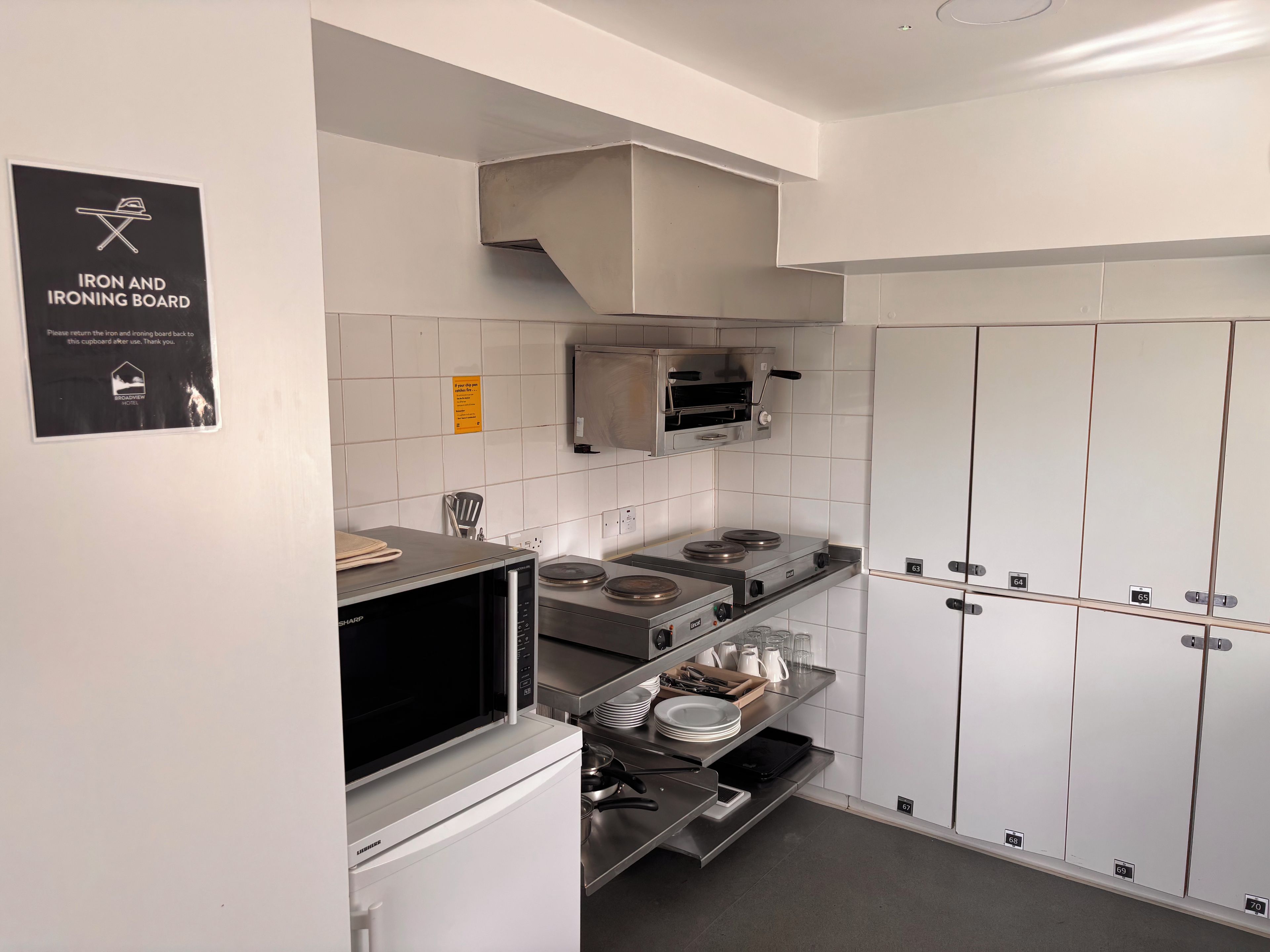 Moderni keittiö, jossa on ruostumattomasta teräksestä valmistetut kodinkoneet, mikroaaltouuni ja sisäänrakennettu uuni. Keittiössä on kyltti, jossa pyydetään palauttamaan silitysrauta ja -lauta.
