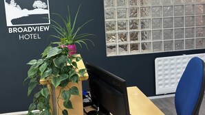 A reception desk with a monitor, a potted plant, and a sign for Broadview Hotel. - Broadview Hotel (Norwich)