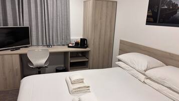 Habitación de hotel con cama, escritorio con computadora, silla, armario y un cuadro en la pared.
