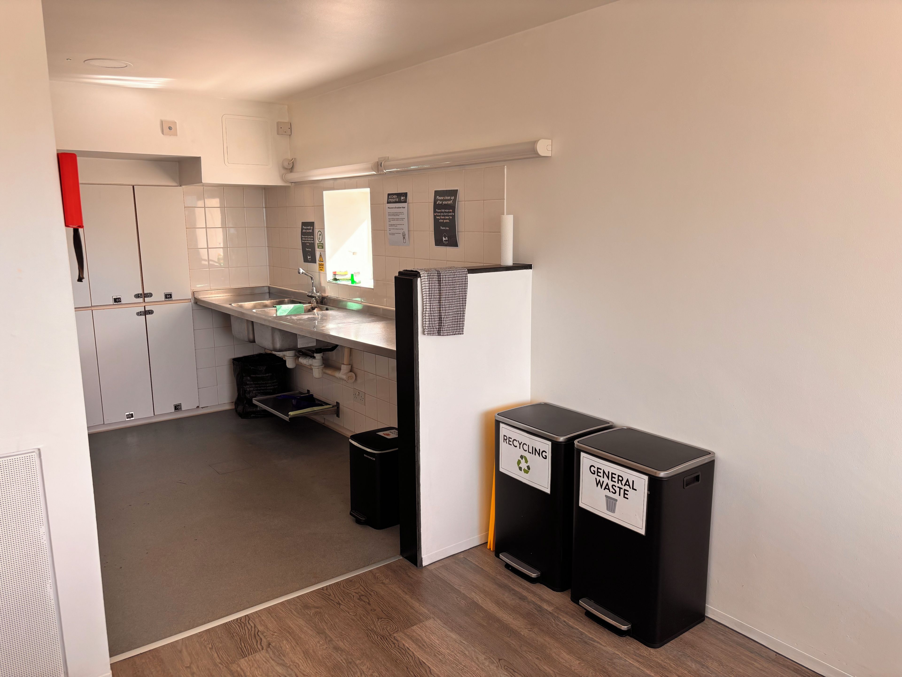 A modern kitchen with a sink, cabinets, and two waste bins labeled for recycling and general waste.