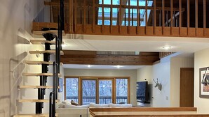 Spazioso loft con tavolo da biliardo, scala in legno e balcone con vista su un paesaggio innevato.