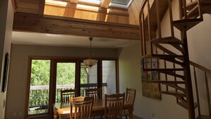 Zona pranzo con tavolo e sedie in legno, un lampadario e vista panoramica attraverso ampie finestre.