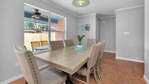 A dining area with a wooden table, beige upholstered chairs, a ceiling fan, and a view of a backyard with a brick wall and outdoor furniture. - No extra Fees for your dogs....Relaxing Family Getaway -3mi to Beach (Navarre)