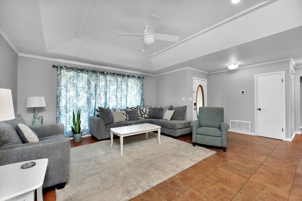 A modern living room with grey sofas, a white coffee table, and a ceiling fan.