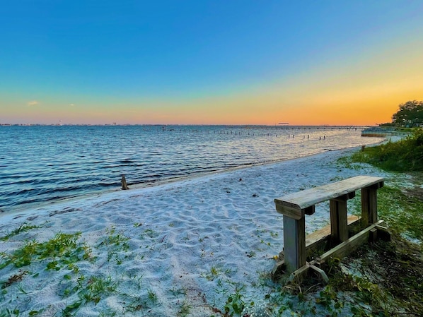 A beach with a wooden bench and a pier in the background.