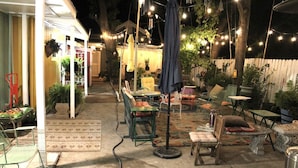 Un área de patio al aire libre con mesas, sillas, luces colgantes y sombrillas.