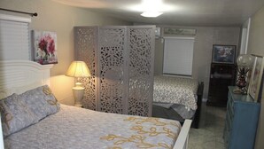 Un dormitorio con cama, mesita de noche, lámpara, cómoda y un biombo decorativo.