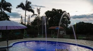 Ein Pool mit Wasserstrahlen, umgeben von Palmen und einem Pavillon.
