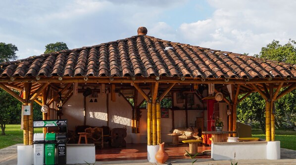 Ein rustikaler Holzpavillon mit Ziegeldach, umgeben von Grün und ausgestattet mit Müllbehältern.