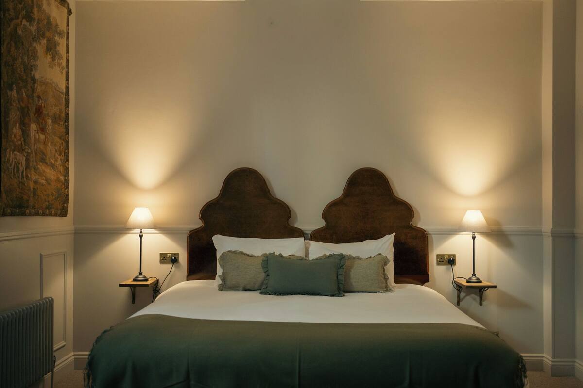 A bed with a headboard, two bedside lamps, and a radiator.