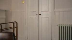 Quarto com duas portas brancas, um radiador e uma cadeira de madeira.