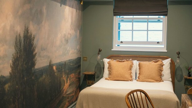 Quarto com um grande mural de paisagem, uma cama com duas almofadas, uma janela com persianas e uma cadeira.