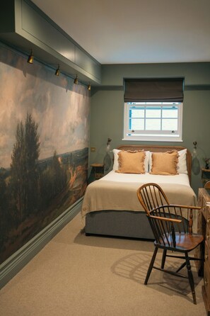 A bedroom with a large landscape mural, a bed with two pillows, a window with blinds, and a chair. - Bower House (London)