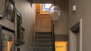 Uma escada com carpete texturizado, um lustre pendurado e quadros nas paredes.