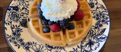A plate with a waffle, whipped cream, raspberries, and blueberries on a floral-patterned plate.