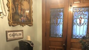 Una puerta de madera con paneles de vitral, un letrero de cafetería, una máquina de café y un cuadro enmarcado en la pared.