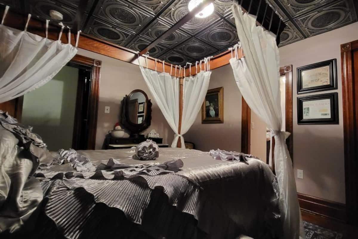 A bedroom with a four-poster bed, a mirror, and framed certificates on the wall.