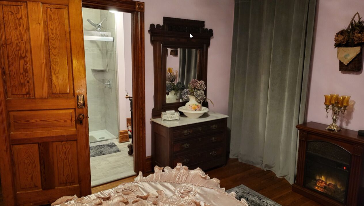 Une pièce avec une porte en bois, un miroir, une commode, une cheminée et un lit recouvert d’une couvre-lit décorative.