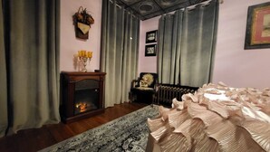 Una habitación con chimenea, una cama con cabecera decorativa, una silla y un tapiz estampado.