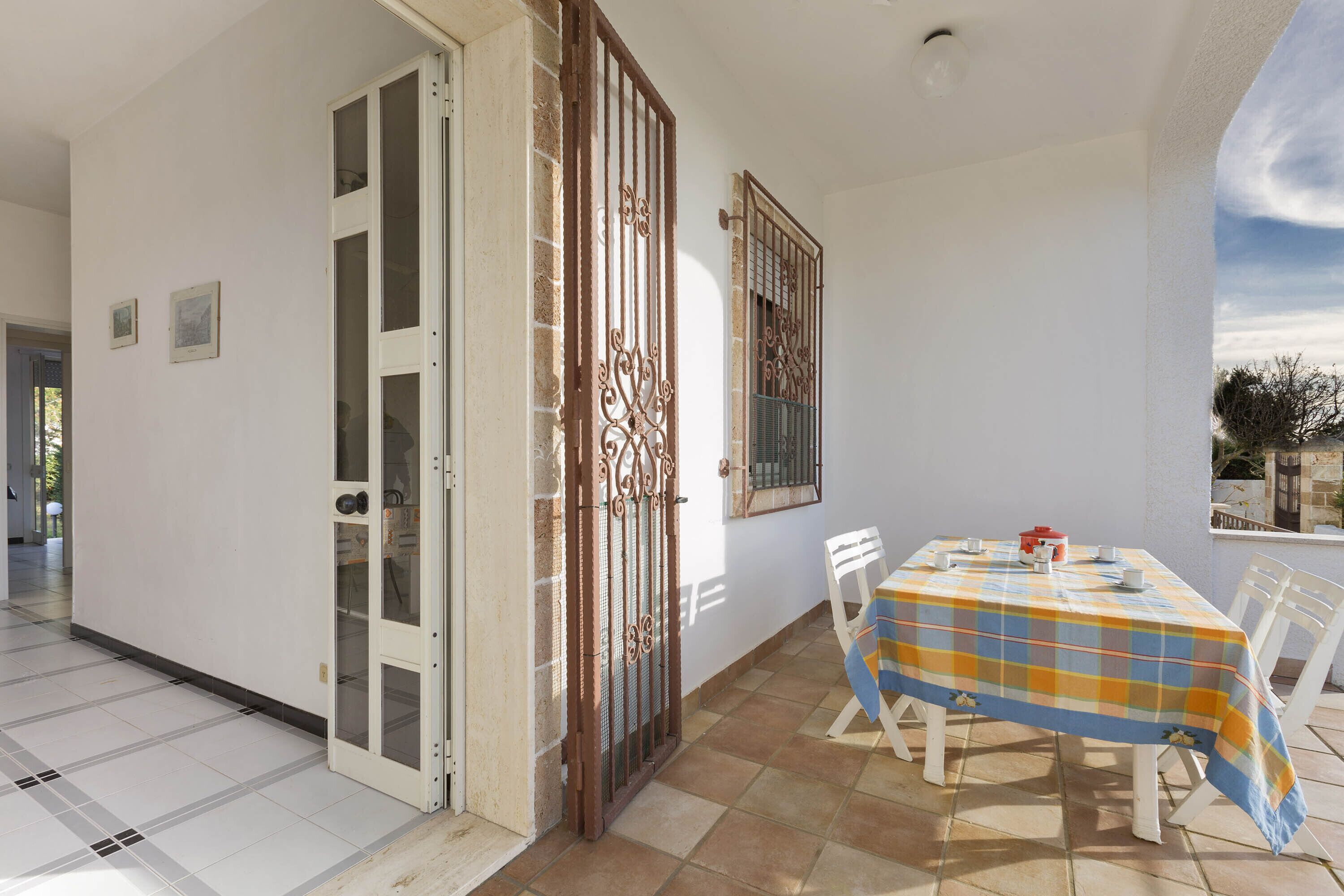 A room with a tiled floor, a table with a checkered tablecloth, and a window with a metal gate.