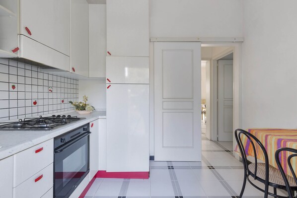 A kitchen with white cabinets, a stove, and a refrigerator. There is a dining area with a table and chairs.