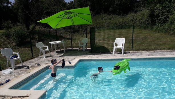 Ein Schwimmbecken mit aufblasbaren Spielzeugen, Stühlen und einem grünen Sonnenschirm.