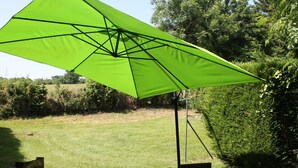 Eine Terrasse mit einem grünen Sonnenschirm, einem Glastisch und Stühlen.