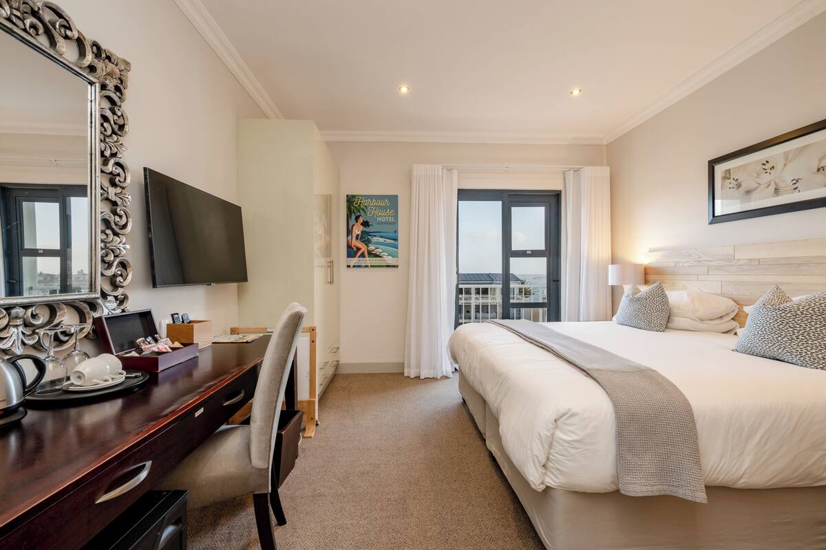 Quarto de hotel com uma cama grande, uma escrivaninha com televisão de tela plana, um espelho grande e uma janela com cortinas.