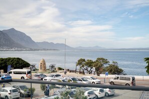 A parking lot with cars, a van, and a monument by the water. - Harbour Square Hotel (Hermanus)