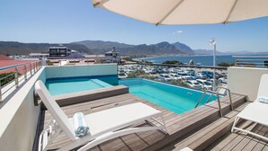 Área de piscina en la azotea con vista al océano y a las montañas, sillas de descanso y zona de estar cubierta.
