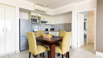 Una cocina moderna con armarios blancos, un refrigerador de acero inoxidable y un microondas. Hay una mesa de comedor con cuatro sillas a rayas y una cesta de fruta.