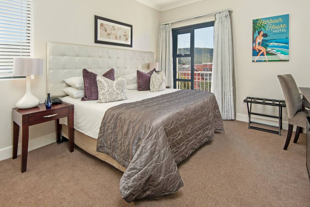 Quarto de hotel com uma cama grande, mesa de cabeceira, escrivaninha e uma cadeira.