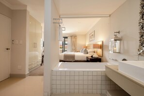 A modern bathroom with a bathtub, a large mirror, and a vanity. - Harbour Square Hotel (Hermanus)