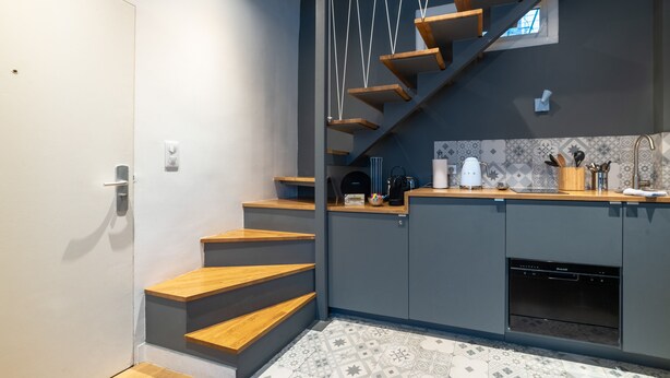 Une cuisine moderne avec des meubles gris, un escalier en bois et un pare-feu en carreaux.