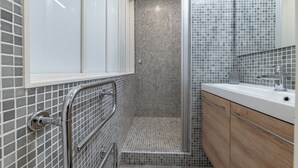 Une salle de bain avec une douche carrelée, une porte de douche en verre, un lavabo blanc et des meubles en bois.