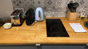 Un plan de travail de cuisine avec un grille-pain, une machine à café et une plaque de cuisson à induction. On y trouve un bol et un torchon.