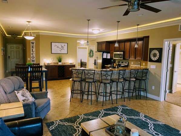 A modern kitchen with a bar area, a dining area with a sofa and chairs, and a living room with a coffee table.