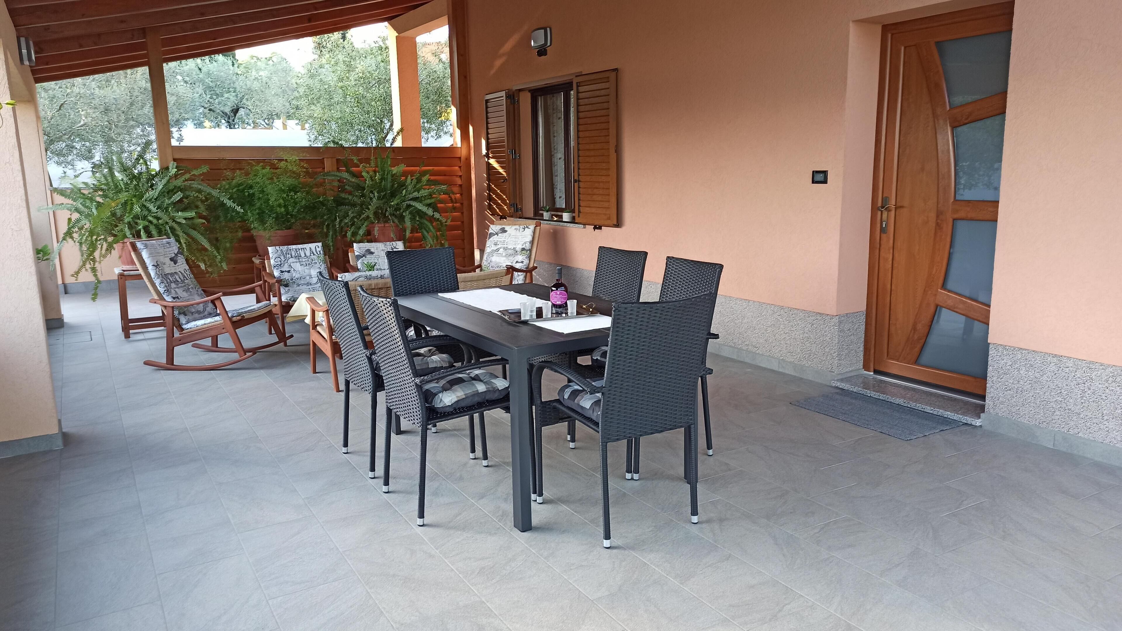 Une terrasse extérieure avec une table et des chaises, entourée de plantes en pot et d’une pergola en bois.
