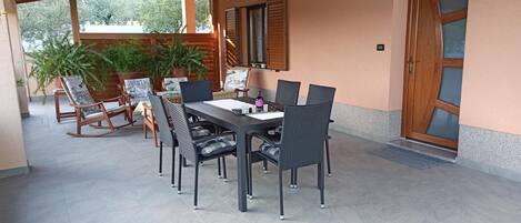 Une terrasse extérieure avec une table et des chaises, entourée de plantes en pot et d’une pergola en bois.