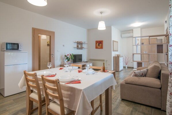 A dining area with a table set for four, a microwave, and a refrigerator in the background. - Apartment with big terrace in nature perfect for a relaxing holiday (Pula)